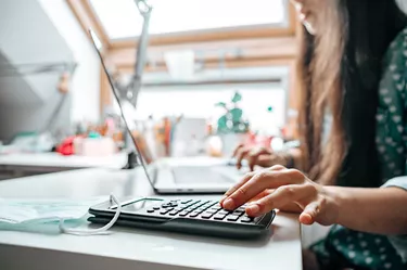 Young woman preparing home budget, using laptop and calculator