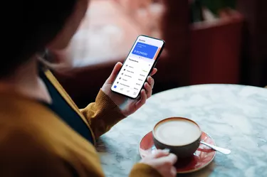 Close-up Shot Of Young Woman Managing Bank Account on Smartphone At Cafe