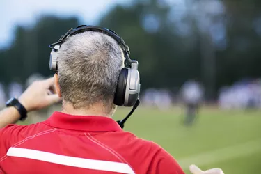 Rear view of American football coach with headphones at playing field