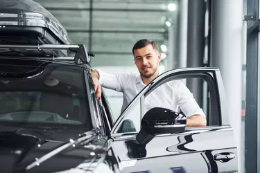 Young man in white shirt is indoors with modern new automobile