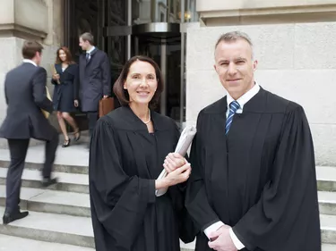 Smiling judges in robes standing outside courthouse