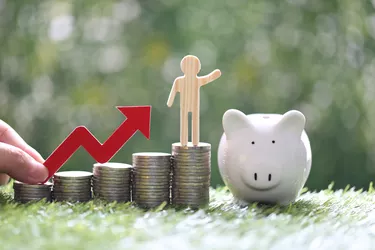 Business man on stack of coins money with hand holding red arrow graph and piggy bank on natural green background, investment and business concept