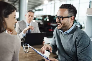 Happy couple talking about contract on a meeting in car showroom.