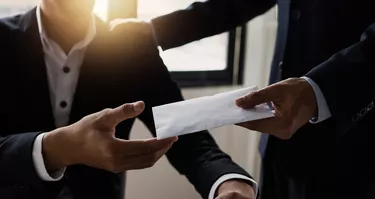 Midsection of businessman giving envelope to colleague at office