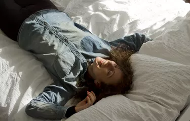 Female Solo Traveller Smiling On Bed In AirBnB