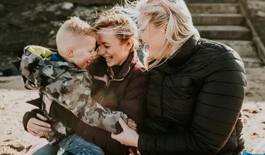 Two woman hold and nuzzle in to a little boy on the beach