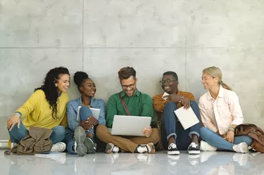 Happy university students using laptop while sitting in a hallway.