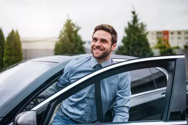 Young man with blue shirt and tie getting out of car in town.