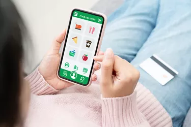 Back rear view of young asian teenage girl in concept next normal life from coronavirus impact using smart phone on hand and pay by credit card at home. Food delivery or grocery order service at home.