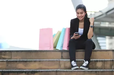 Cheerful young Asian woman looking mobile smart phone at outdoors. Shopping online concept.