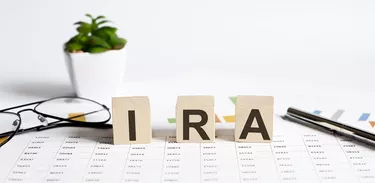 IRA word concept written on the wooden blocks, cubes on a light table with flower ,pen and glasses on chart background