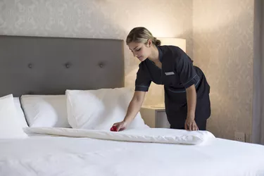 Chambermaid making bed in hotel room