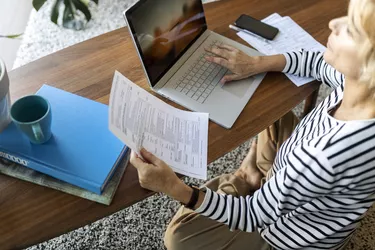 Mature woman with documents using laptop at home