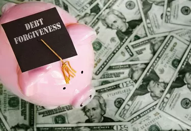 Piggy bank with Debt Forgiveness graduation cap on cash