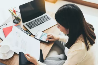 Young asian woman use calculator to calculate expenses, business profit, loss account and work on paperwork at home. Businesswoman working on small desk while sitting at living room selective focus