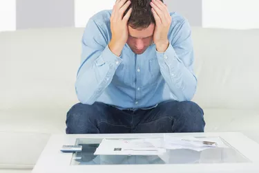 Frustrated casual man sitting on couch paying bills