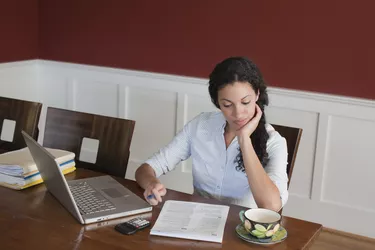 Woman Working on Laptop Computer, Calculator and Tax Documents at Dining Room Table