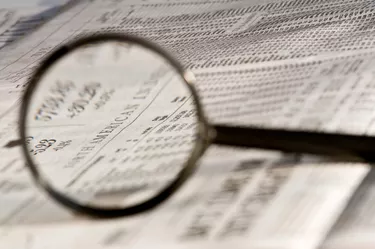 Magnifying glass highlighting investment stock quotes in business section of newspaper.