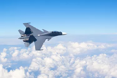 Combat fighter jet flies turning maneuver high in the sky above the clouds.