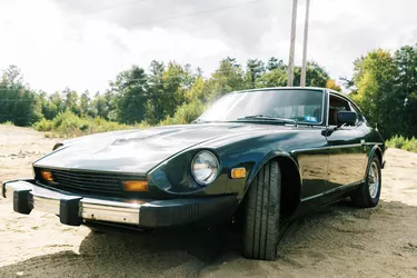 Green classic Japanese muscle car parked in sand lot in sunshine
