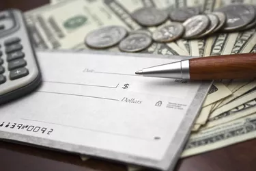 Close-up of blank check, US bills/coins, calculator and pen